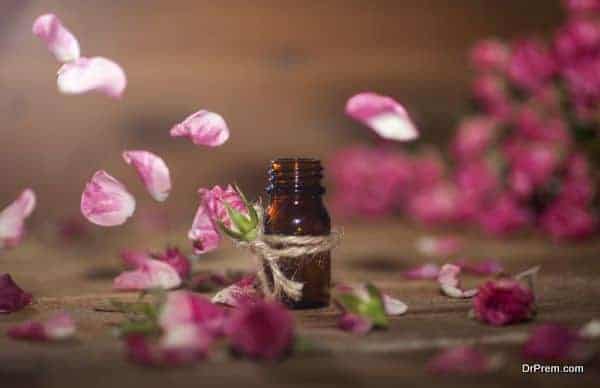 Closeup of bottle with rose essential oil with falling leaves on wooden background.