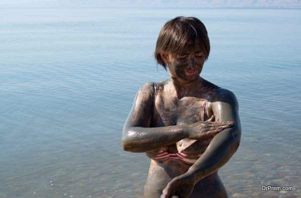 Woman applying Dead Sea mud body care treatment