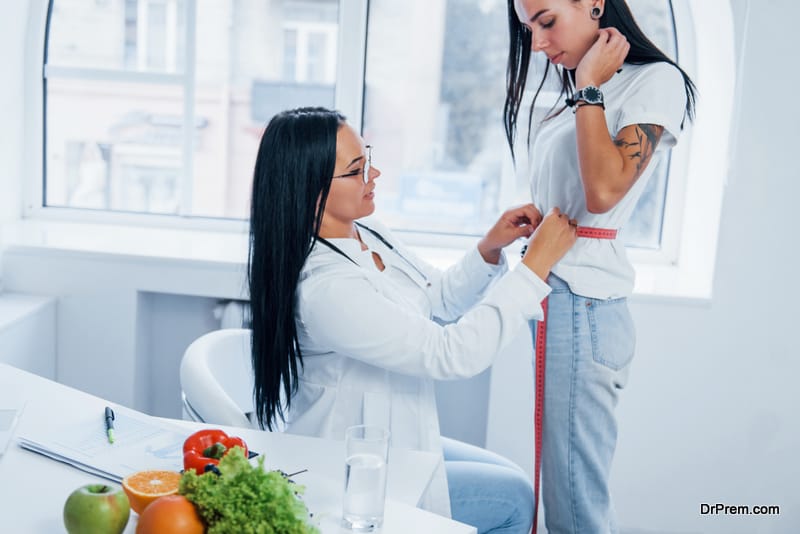 Female nutritionist measuring waist of patient by tape indoors in the office.