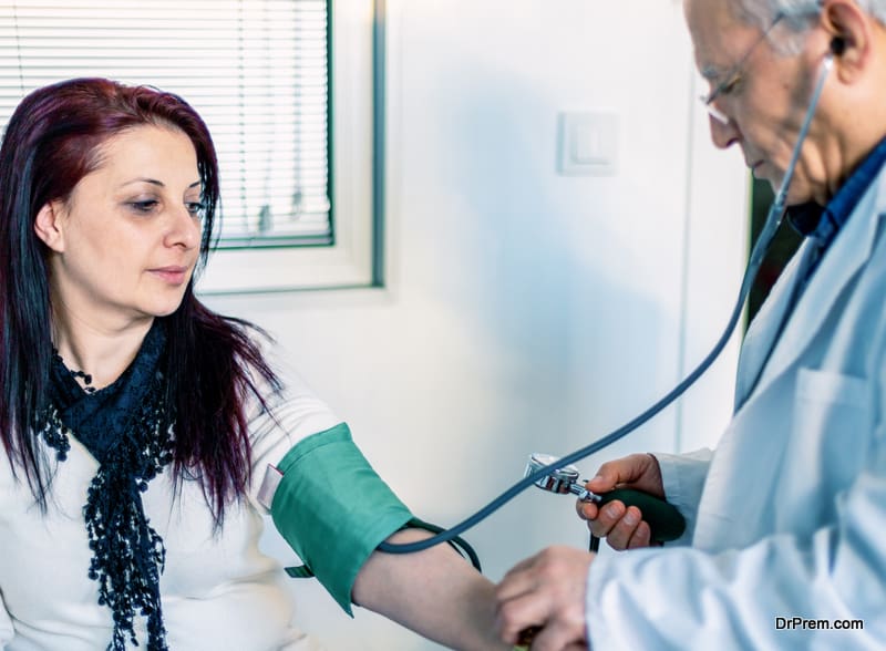 Doctor checking female patient's blood pressure in examination room