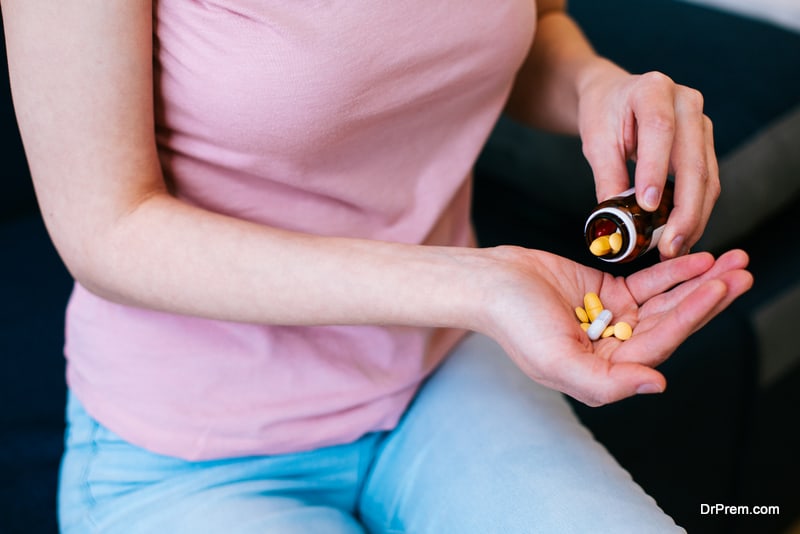 Unrecognized young woman sitting alone and getting several pills from the glass bottle