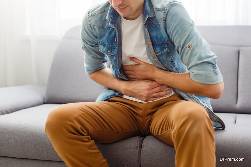 The man is sitting on a gray couch and holding his belly