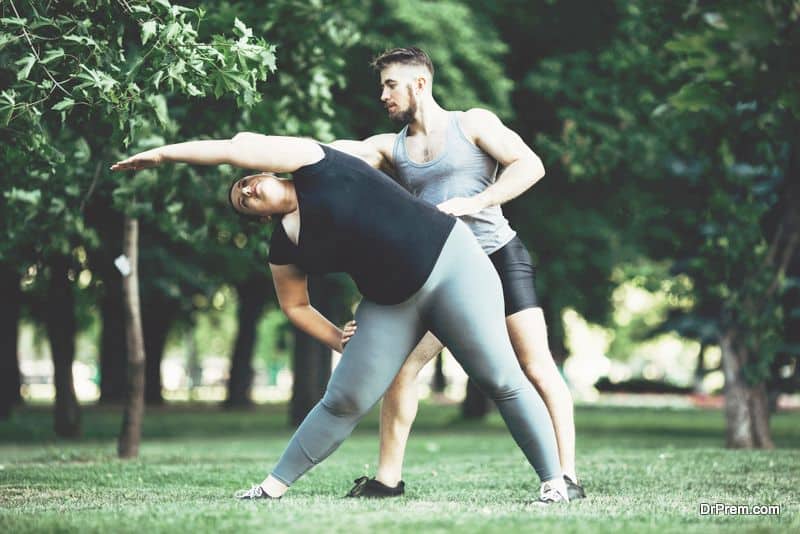 Personal trainer correct his client while doing stretching exercise. Overweight woman doing yoga with instructor support.