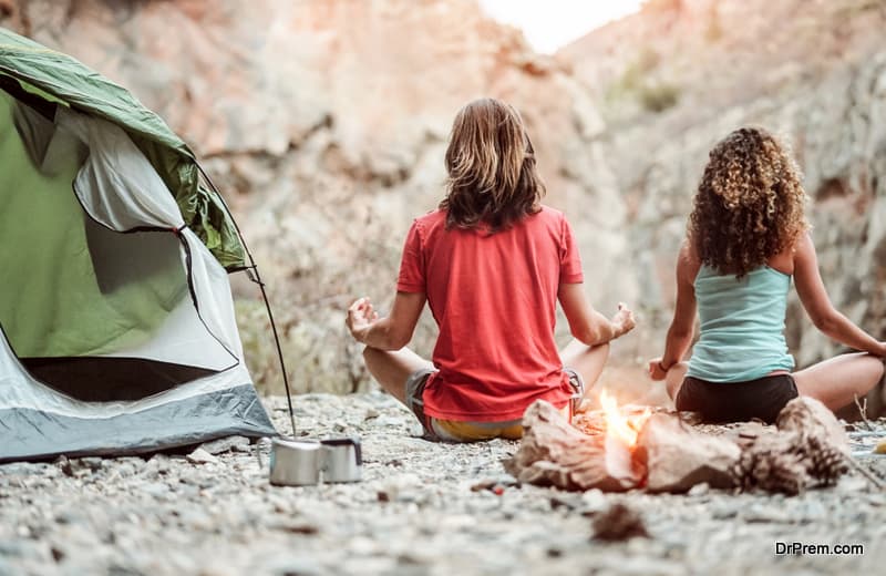 Young couple meditating together while camping on mountains - Healthy people training mind with meditate exercises - Youth expression culture and health lifestyle concept