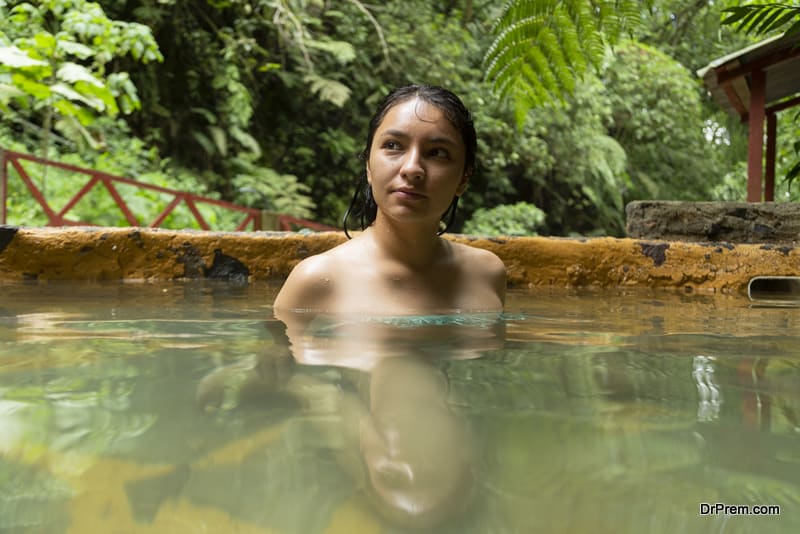 Hispanic woman relaxing in hot springs surrounded by tropical nature