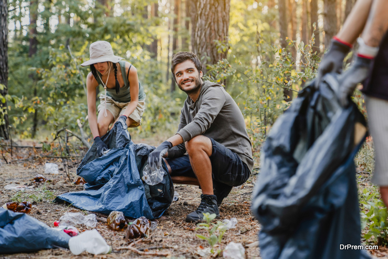 Young man looking on his friend while collecting trash and plastic in forest