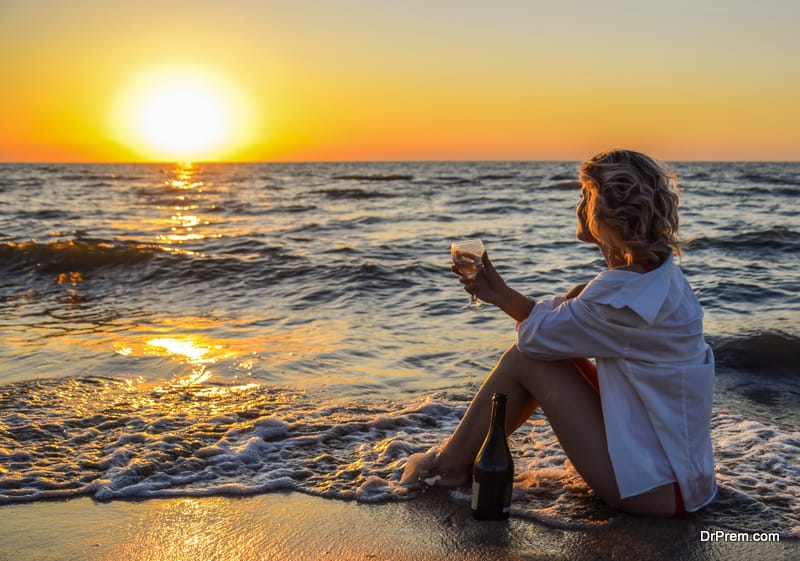 Girl with a glass and a bottle of champagne sits on the seashore.