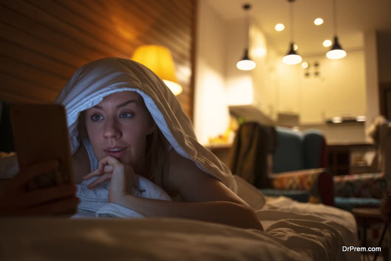 Woman using her phone under blanket in bed at night