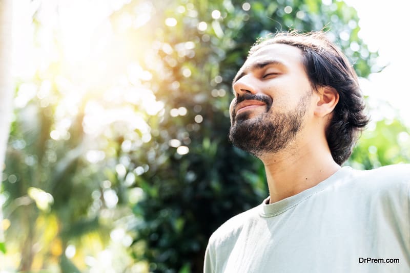 A bearded man is meditating outdoor in the park with face raised up to sky and eyes closed on sunny summer day. Concept of meditation, dreaming, wellbeing and healthy lifestyle