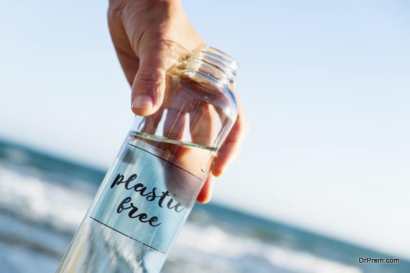 closeup of a caucasian man holding a glass reusable water bottle with the text plastic free written in it, on the beach