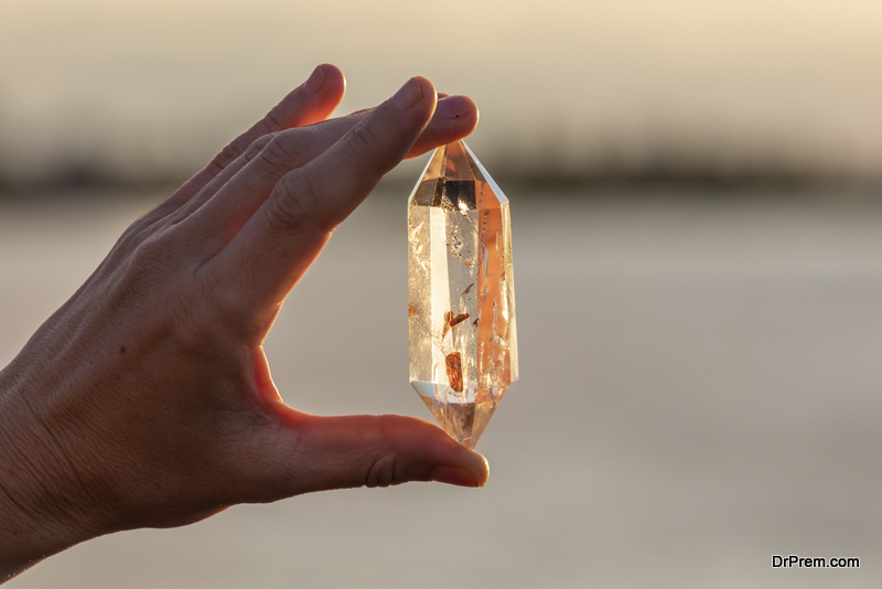 A hand holding up a beautiful quartz crystal outdoors in the sun
