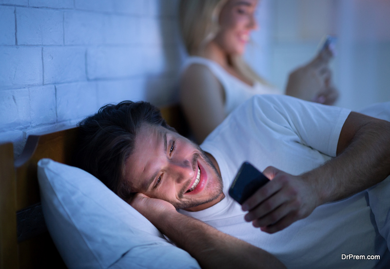 Husband Texting On Mobile Phone Lying With Wife In Bedroom
