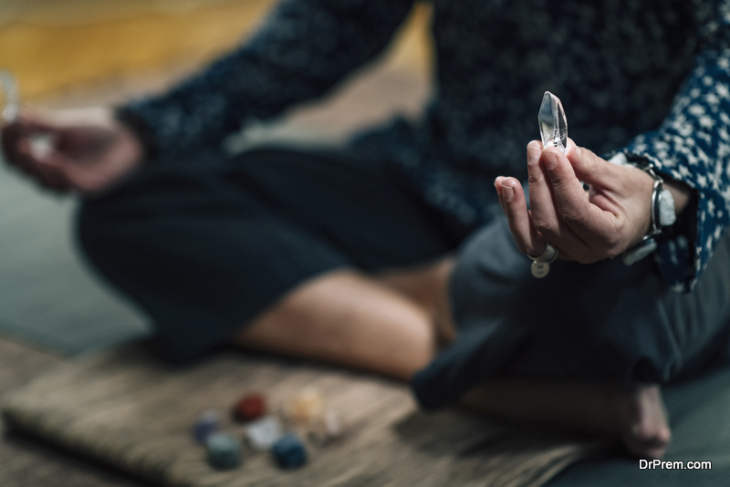 Woman meditating with crystals in lotus position at home. Quartz crystals chakra wands in female hands.