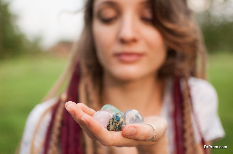 Young beautiful girl with long dreadlocks holds in hands 5 natural stones rose quarz, rhinestone, angelite, anyolite, and azurite outdoors during morning, mineralogy concept