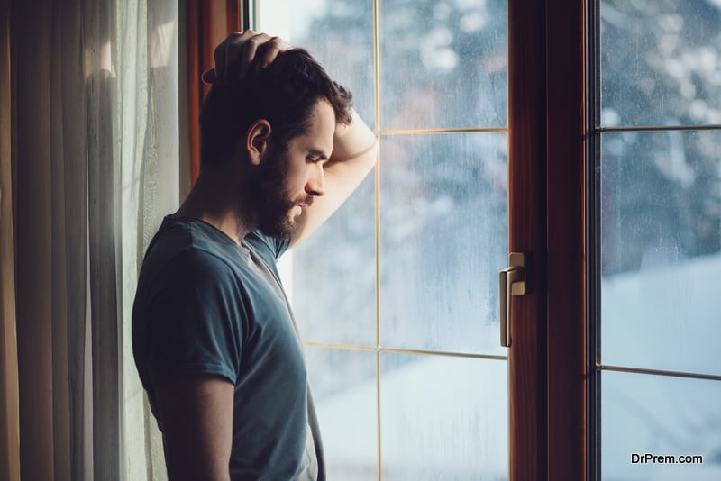 Young sad man sitting by the window in regret