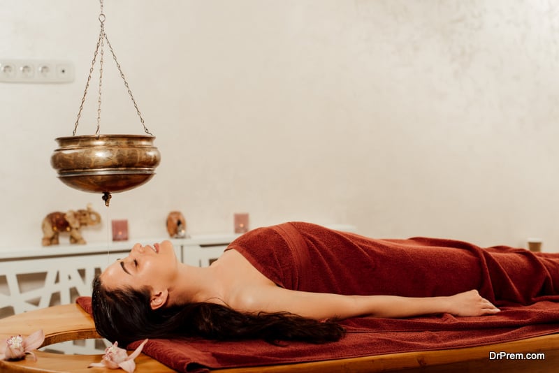 side view of woman lying under shirodhara vessel during ayurvedic procedure