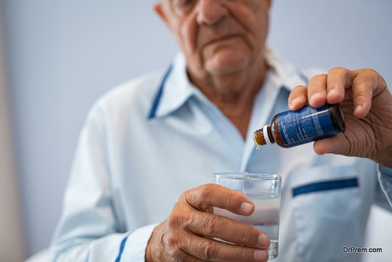 Close up of wrinkled hands of senior man pouring melatonin drops in glass of water 