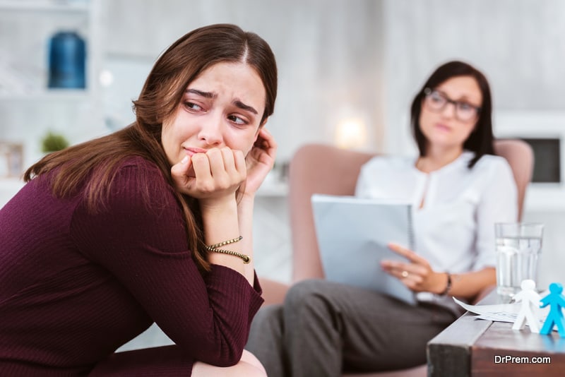 Unhappy depressed woman turning her head and almost crying while a calm psychologist looking at her