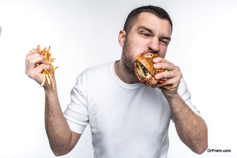 This guy is very delight of junk food. He is biting a big piece of burger and holding a full hand of french fries covered with ketchup. Young amn likes to eat oily meal. Isolated on white background