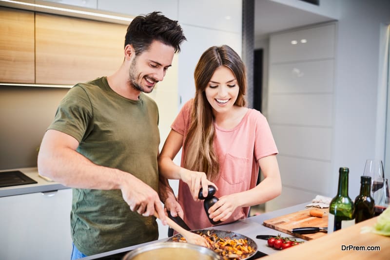Cute joyful couple cooking together and adding spice to meal, laughing and spending time together in the kitchen