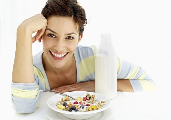 portrait of a young woman sitting with a bowl of breakfast cereal and milk