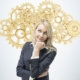 Beautiful blonde business woman is thinking about optimisation of the business process. A concept of business management solutions. Golden gears as a cloud.