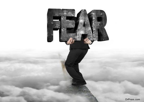 Man carrying big 3D fear concrete word balancing on ridge with with gray cloudy sky background