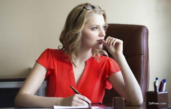 Attractive young elegant smart blonde working business woman sitting in office on brown leather chair in red blouse and glasses thinking and writing looking away indoor on white background, horizontal picture